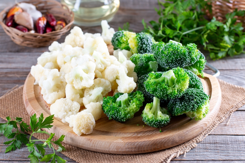 Frozen produce cauliflower and broccoli on a cutting board on a wooden table
